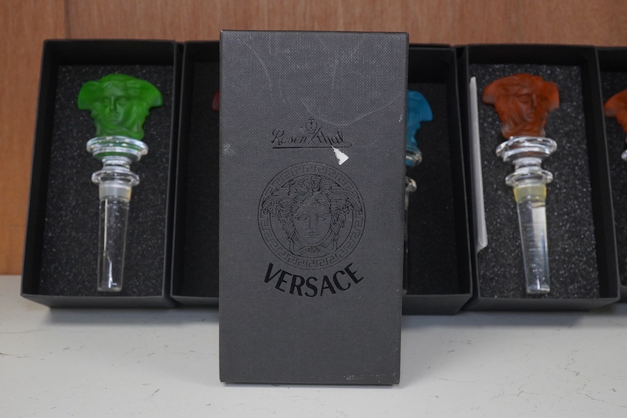 Six boxed Rosenthal for Versace glass Medusa head wine bottle stoppers in various colours and a boxed miniature timepiece, 8.5cm high (7). Condition - good.